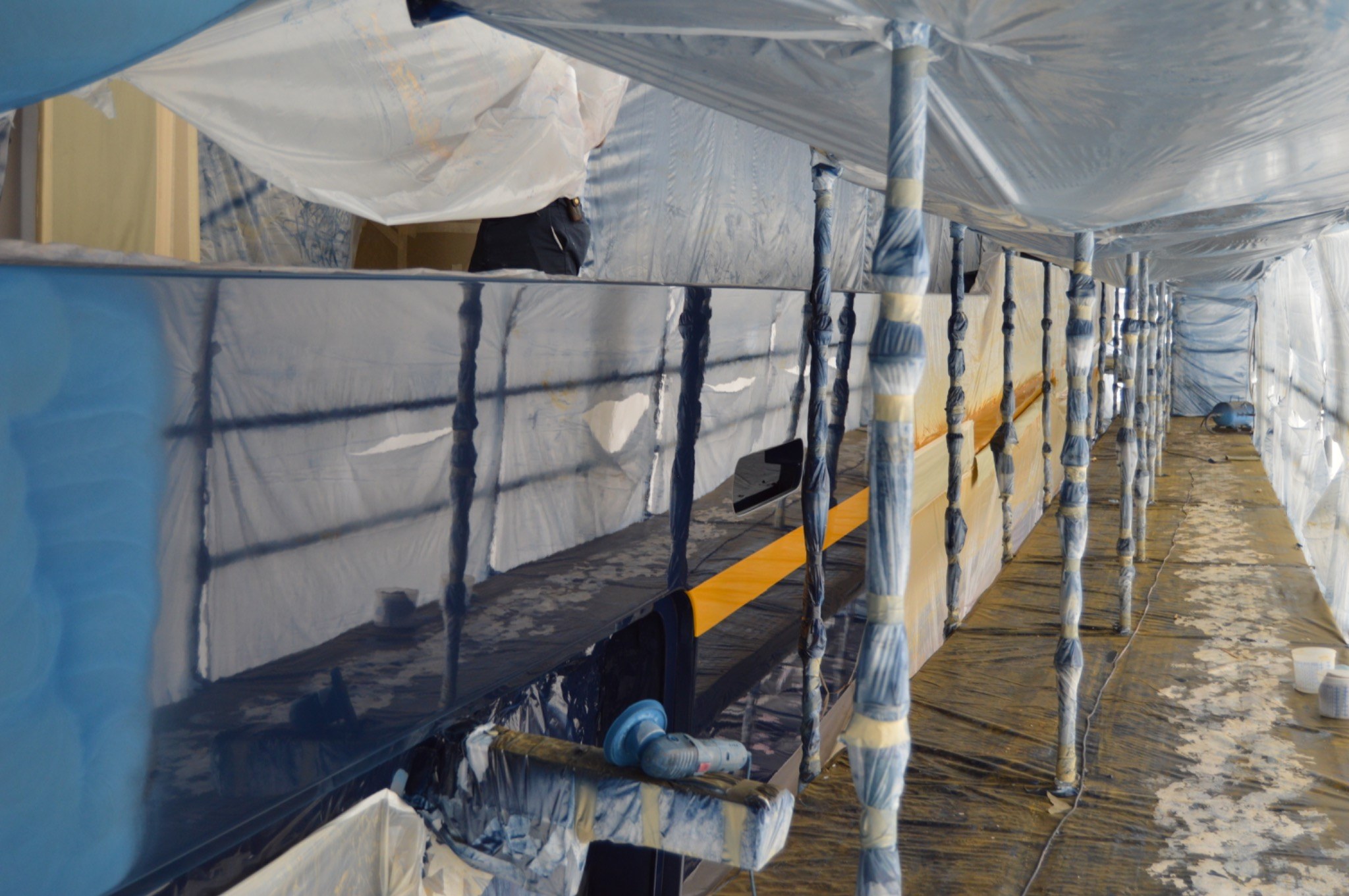 Large yacht hull surrounded by scaffold and protective sheeting during coating work