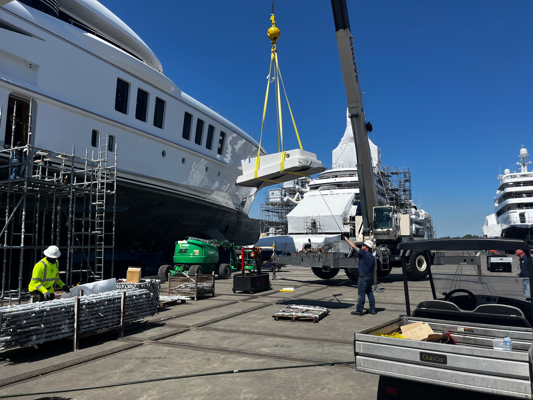 Shipyard crane lifting a large yacht component beside major motor yachts